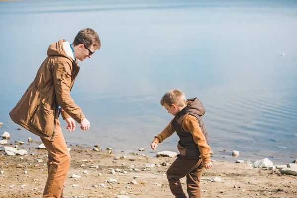 Père enseignant petit fils jeter des pierres dans l'eau — Photo
