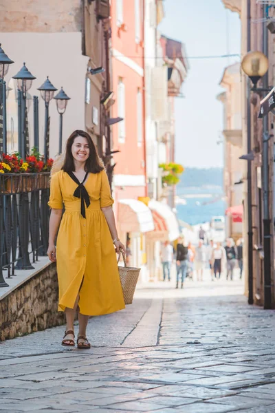 Mladá krásná žena ve žlutých šatech, po malých uličkách v ulicích města na pozadí — Stock fotografie