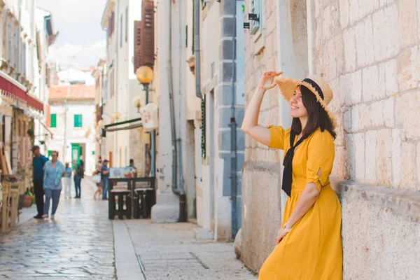 Женщина в летнем желтом платье с шляпой, стоящей возле каменного здания в летнем курортном городе — стоковое фото