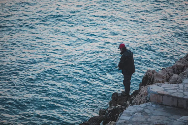 ROVINJ, CROÁCIA - 22 de maio de 2019: homem sentado na falésia e pescando no mar — Fotografia de Stock