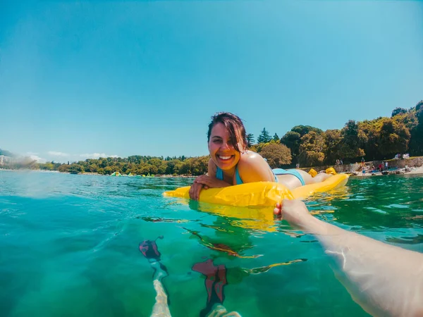 Žena na žluté nafuatelné matraci v rukou vody, která drží její pohled — Stock fotografie