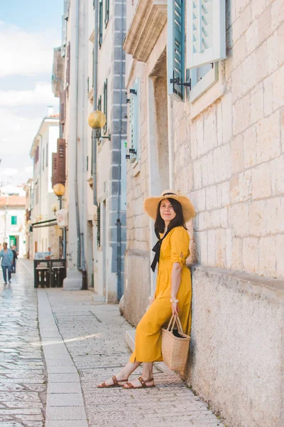 Mulher no verão vestido amarelo com chapéu de pé perto de pedra edifício na cidade resort de verão — Fotografia de Stock