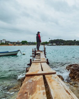 fırtınalı denize bakan küçük balıkçı iskelesinin kenarında duran adam