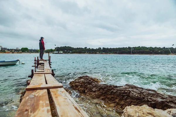 Homem de pé na borda do pequeno cais de pesca olhando para o mar tempestuoso — Fotografia de Stock