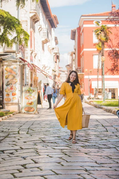 Žena ve žlutých šatech s kouskem slaměných klobouků, procházky po starém turistickém městě v Chorvatsku — Stock fotografie