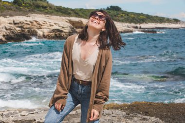 Deniz kıyısında doğanın gücünün tadını çıkaran bir kadın. Rüzgarlı hava