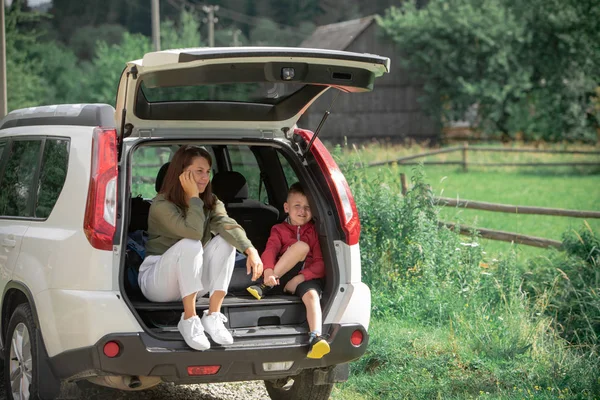 Молода мати з хлопчиком сидить у багажнику, відпочиває в літній сонячний день — стокове фото