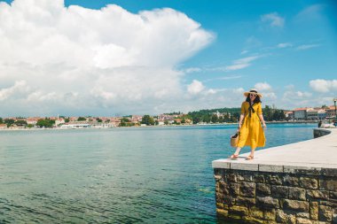 taş kenarı iskelede duran kadın denize bakıyor. sarı sundress