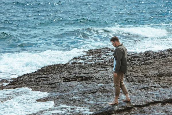 風の強い夏休みに岩のビーチを歩く男。海の景色を楽しむ — ストック写真