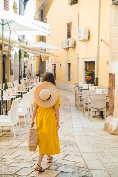Žena ve žlutém oděvu pěšky po městské ulici mezi kavárenskými restauratními stolky — Stock fotografie