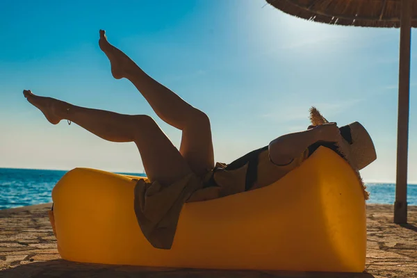 Femme en robe de soleil jaune posée sur un canapé jaune à la plage de la mer — Photo