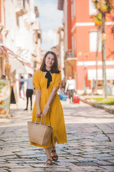 Žena ve žlutých šatech s kouskem slaměných klobouků, procházky po starém turistickém městě v Chorvatsku — Stock fotografie