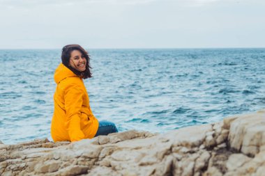 Uçurumun kenarında oturan kadın büyük dalgalara bakıyor.