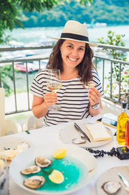 Açık havada Restoran istiridye ve içme şarabı yeme oturan Fedora şapka gülümseyen güzel kadın