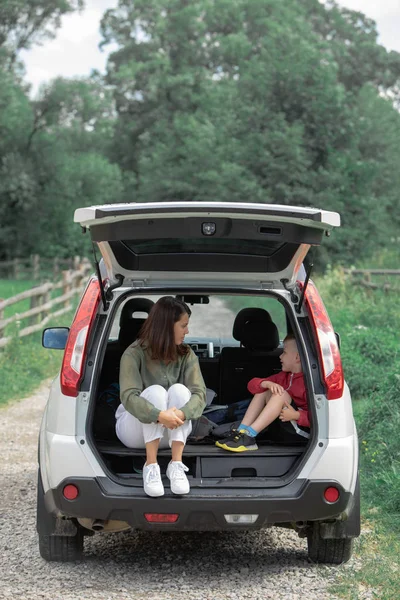 Young mother with kid boy sitting in car trunk resting in summer sunny day — Stock Photo, Image