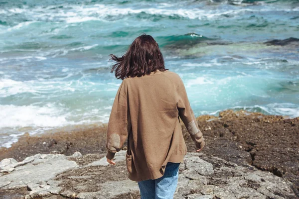 Mulher andando pela praia de mar rochoso no dia ensolarado ventoso. férias de verão — Fotografia de Stock
