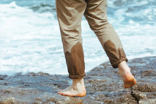 Deniz kıyısında yürüyen pantolonlu ıslak adam bacakları. Kayalık plajda suyun tadını çıkarıyor.