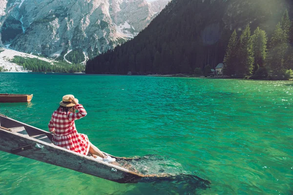 Woman sitting on stairs in red dress and straw hat near lake in mountains — Stock Photo, Image