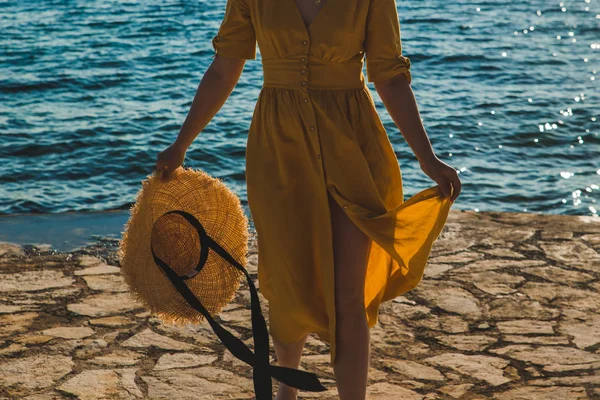young pretty smiling woman in yellow sundress walking by stone beach