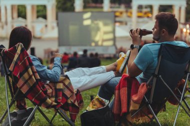 Açık havada sinemada Şehir Parkı görünümlü sinema salonu içinde kamp sandalyeleri oturan çift