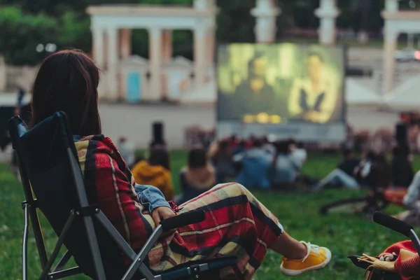 Mulher comendo batatas fritas sentado na cadeira de acampamento olhando filme no cinema ao ar livre — Fotografia de Stock