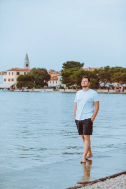 Hırvatistan 'da arka planda yaz akşamı Fazana kasabasında deniz Plajı ile yürüyen adam