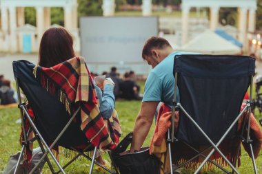 Açık havada sinemada Şehir Parkı görünümlü sinema salonu içinde kamp sandalyeleri oturan çift