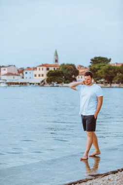 Hırvatistan 'da arka planda yaz akşamı Fazana kasabasında deniz Plajı ile yürüyen adam