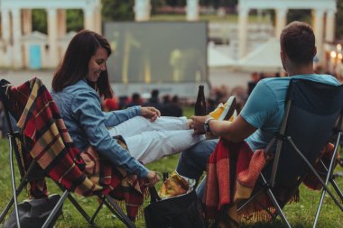 Açık havada sinemada Şehir Parkı görünümlü sinema salonu içinde kamp sandalyeleri oturan çift