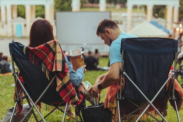 Ζευγάρι κάθονται σε κατασκηνώσεις-καρέκλες στο πάρκο της πόλης αναζητούν ταινία σε εξωτερικούς χώρους στον υπαίθριο κινηματογράφο — Φωτογραφία Αρχείου
