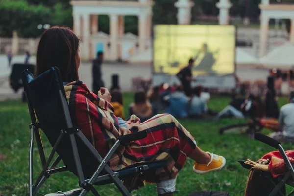 Woman eating chips sitting in camp-chair looking movie in open air cinema — Stock Photo, Image