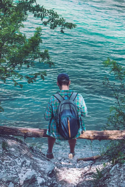 man with backpack sitting at wood log enjoying water view