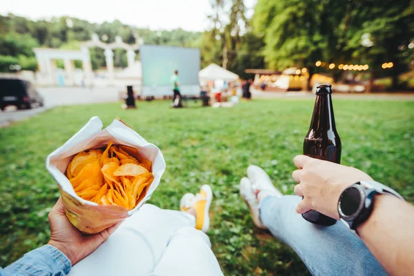 Homem mão segurando garrafa de cerveja mulher mão segurando chips ao ar livre cinema — Fotografia de Stock