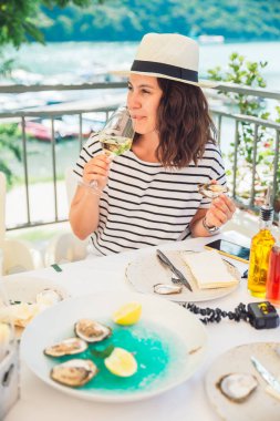 Açık havada Restoran istiridye ve içme şarabı yeme oturan Fedora şapka gülümseyen güzel kadın