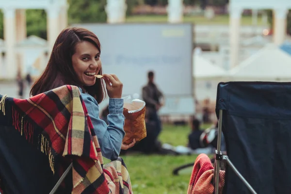 Woman eating chips sitting in camp-chair looking movie in open air cinema — Stock Photo, Image