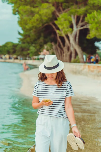 Donna in abiti bianchi e cappello fedora passeggiando sulla spiaggia di mare — Foto Stock