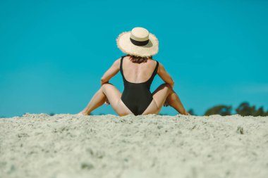 kum plajda oturan Siyah mayo kadın arkasında görünümü
