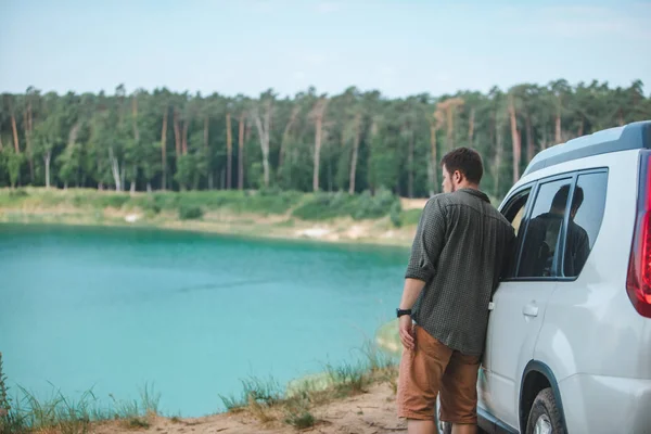 Hombre cerca de coche suv blanco en el borde mirando al lago con agua azul — Foto de Stock