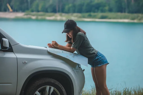 Kobieta sprawdzanie z mapą na SUV samochód kaptur jezioro z błękitną wodą na tle — Zdjęcie stockowe