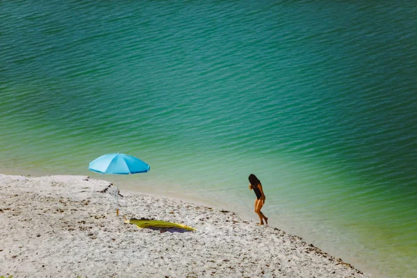 Mujer en traje de baño caminando por la playa de arena sombrilla azul y manta amarilla — Foto de Stock