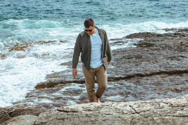 Rüzgarlı yaz tatilinde Rocky Beach 'te yürüyen bir adam. Deniz manzarasının tadını çıkar