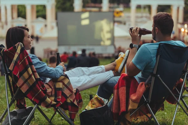 Ζευγάρι κάθονται σε κατασκηνώσεις-καρέκλες στο πάρκο της πόλης αναζητούν ταινία σε εξωτερικούς χώρους στον υπαίθριο κινηματογράφο — Φωτογραφία Αρχείου