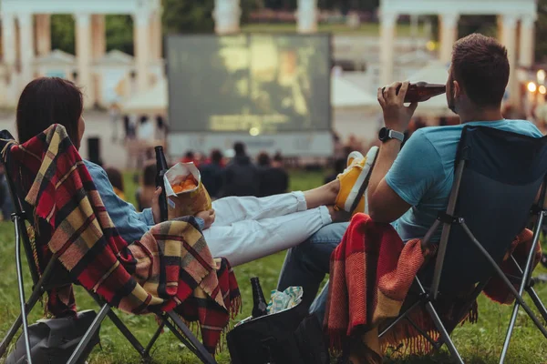 Açık havada sinemada Şehir Parkı görünümlü sinema salonu içinde kamp sandalyeleri oturan çift