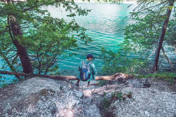 Man with backpack sitting at wood log enjoying water view — Stock Photo, Image