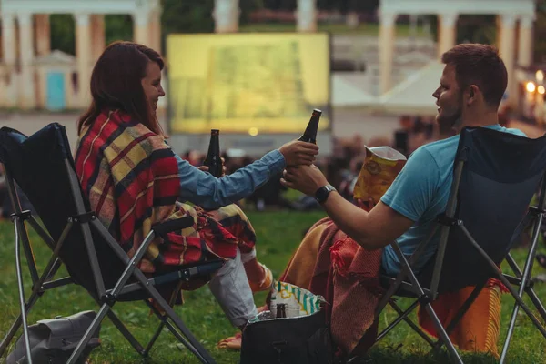 Couple sitting in camp-chairs in city park looking movie outdoors at open air cinema — Stock Photo, Image