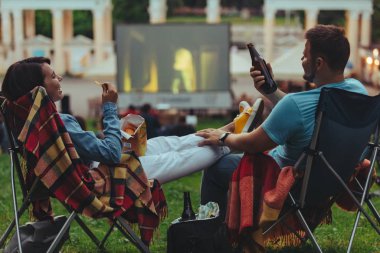 Açık havada sinemada Şehir Parkı görünümlü sinema salonu içinde kamp sandalyeleri oturan çift