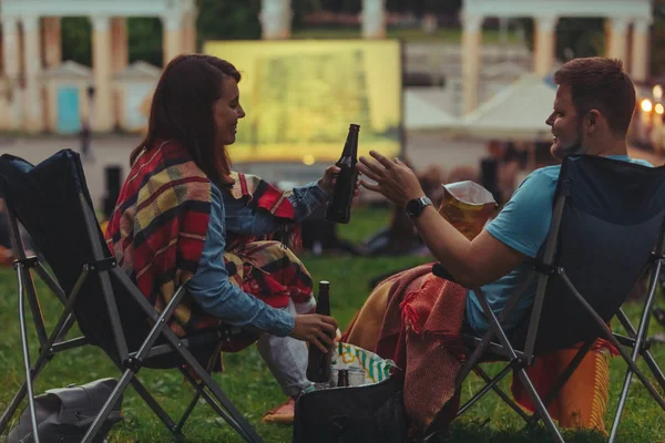 Couple sitting in camp-chairs in city park looking movie outdoors at open air cinema — Stock Photo, Image