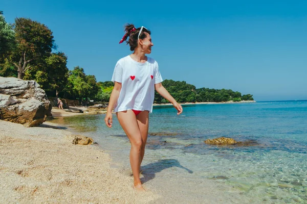 Sexy Frau in rotem Badeanzug und weißem T-Shirt am Meeresstrand — Stockfoto