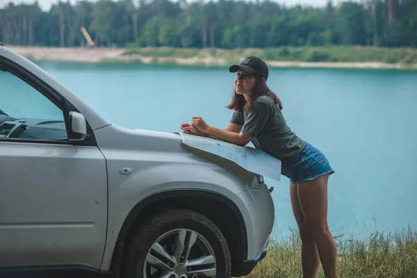 Mujer que comprueba con el mapa en el lago capucha coche suv con agua azul en el fondo — Foto de Stock