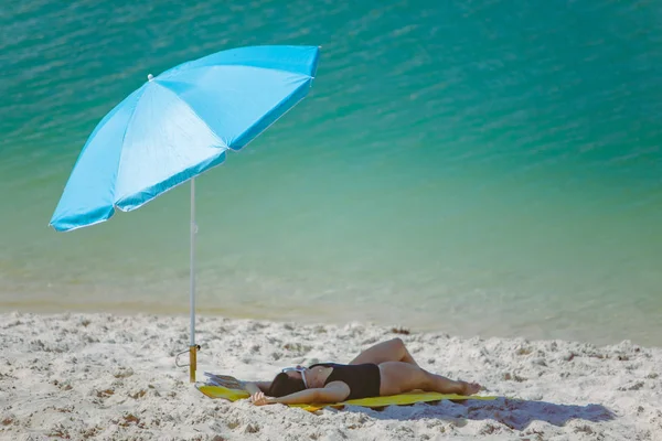 Žena v plavkách chůze písečnou pláží modrý sluneční deštník a žlutá přikrývka — Stock fotografie